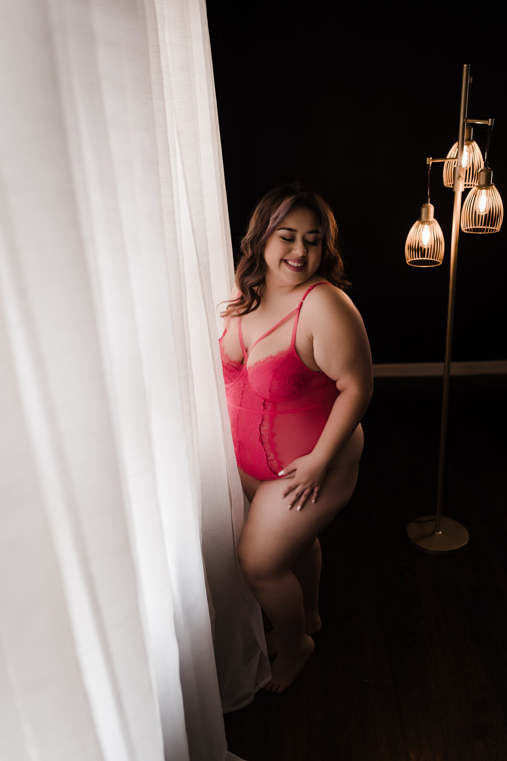 Woman stands in pink lingerie next to a white curtained window eden spa memphis