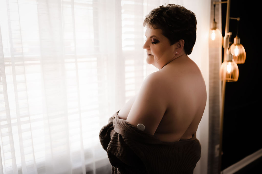 A woman wrapped in a dark blanket stands in front of a window looking down her shoulder living health day spa