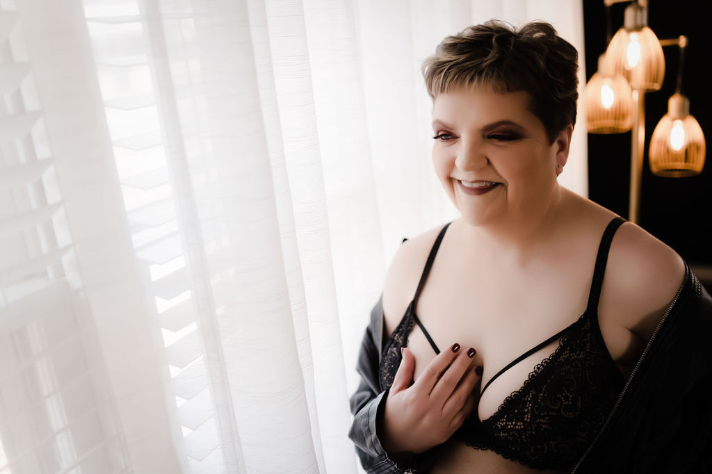 A woman in black lace lingerie stands in front of a large window