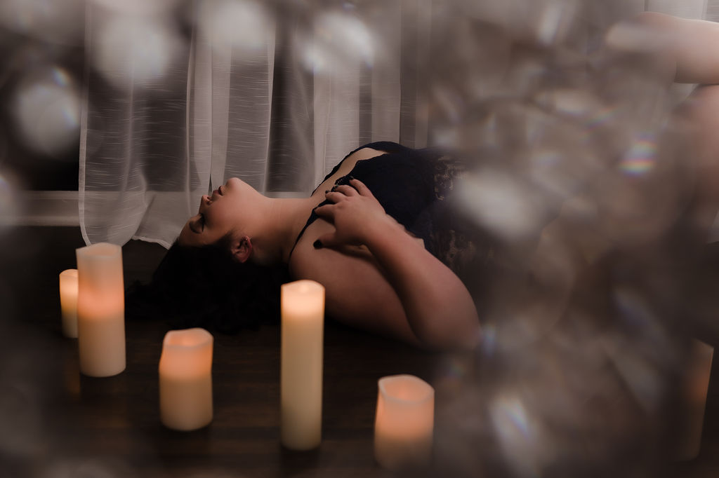 A woman in black lingerie lays on the floor around some candles memphis microblading