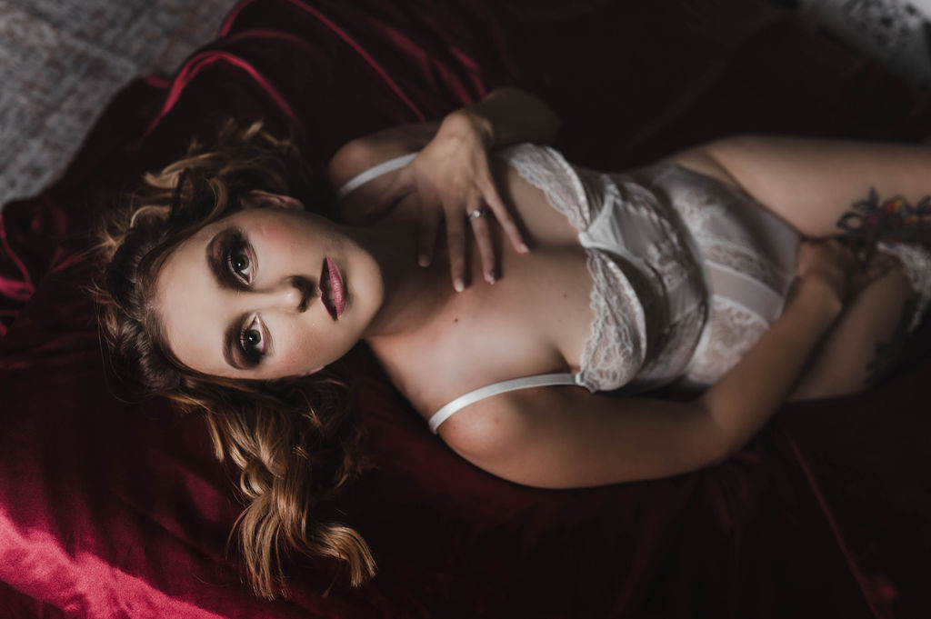 A woman in white lace lingerie leans back on a red couch with a hand on her chest after visiting a makeup artist jonesboro ar