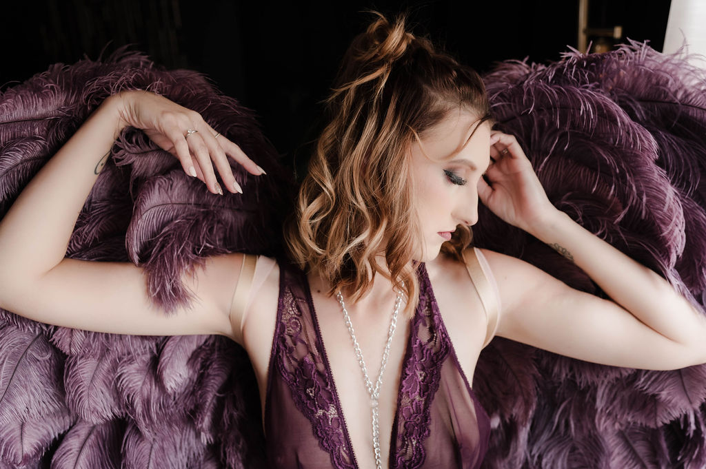 A woman stands in lace lingerie and large purple feather wings