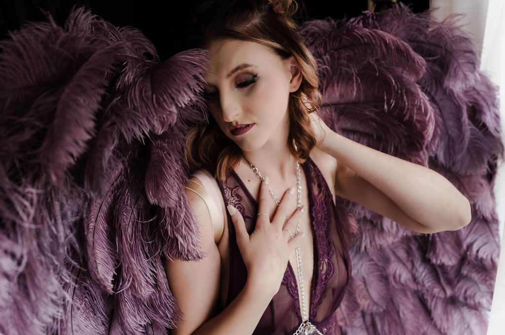 A woman wears lace purple lingerie and matching large feather wings while standing in a window after some brunch jonesboro ar