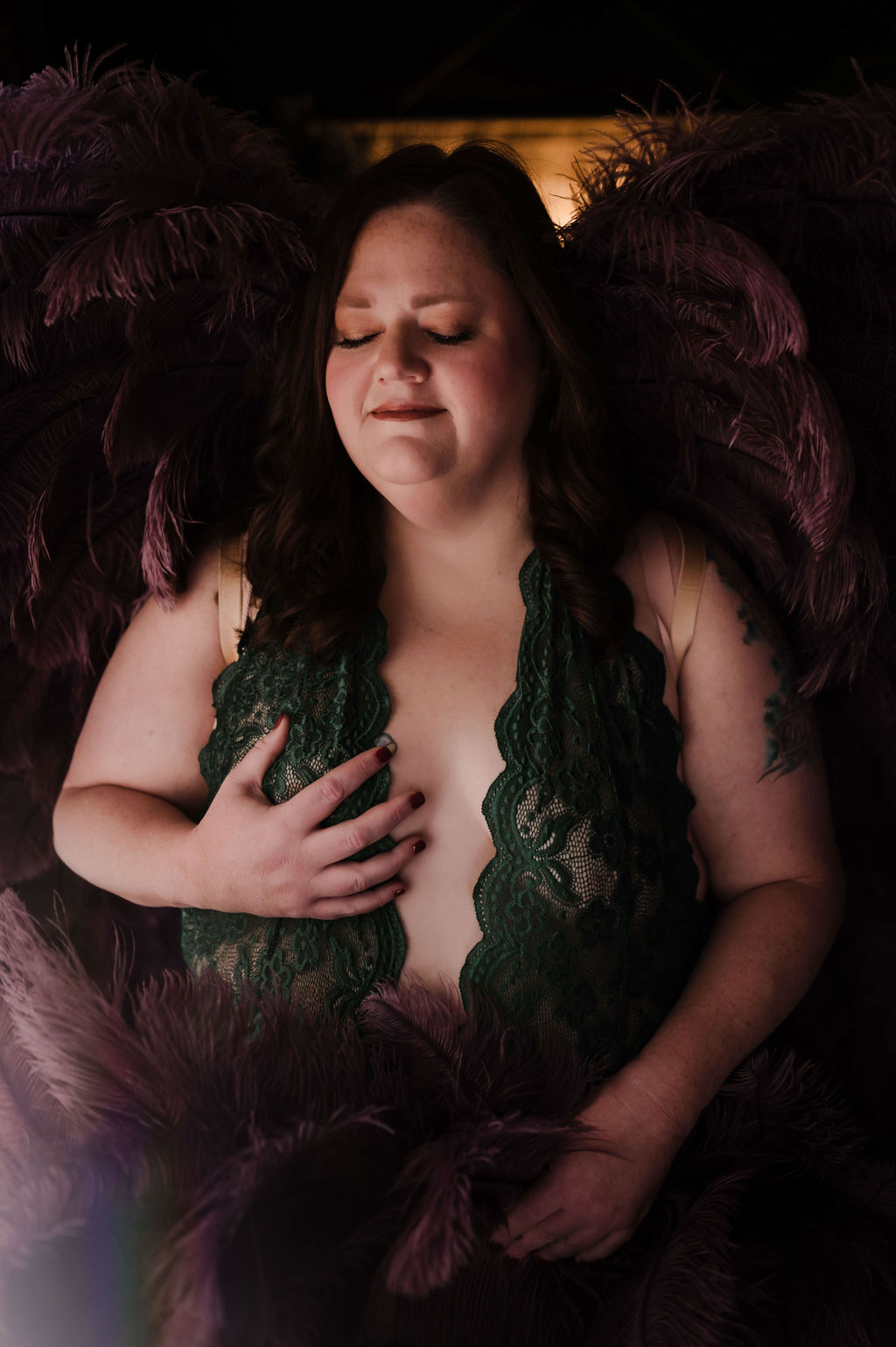 A woman stands in a studio wearing green lace lingerie and large purple feather wings