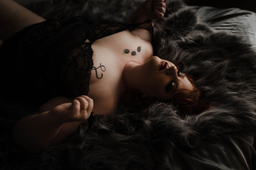 A woman in black lace lingerie lays on a bed in a studio on a fur blanket with eyes closed after some yoga jonesboro ar