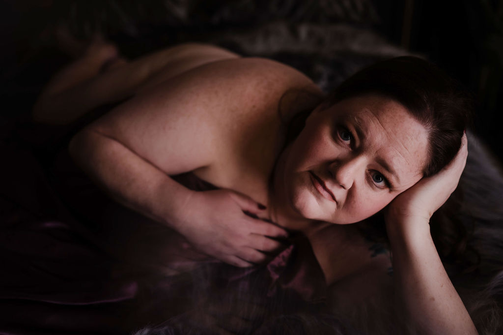 A woman rests her head on her hand while laying across a maroon bed in a studio after visiting spas hernando ms