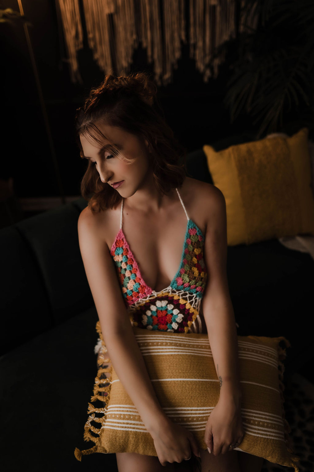 A woman in a knit bra sits on a couch with a pillow in her lap in a studio