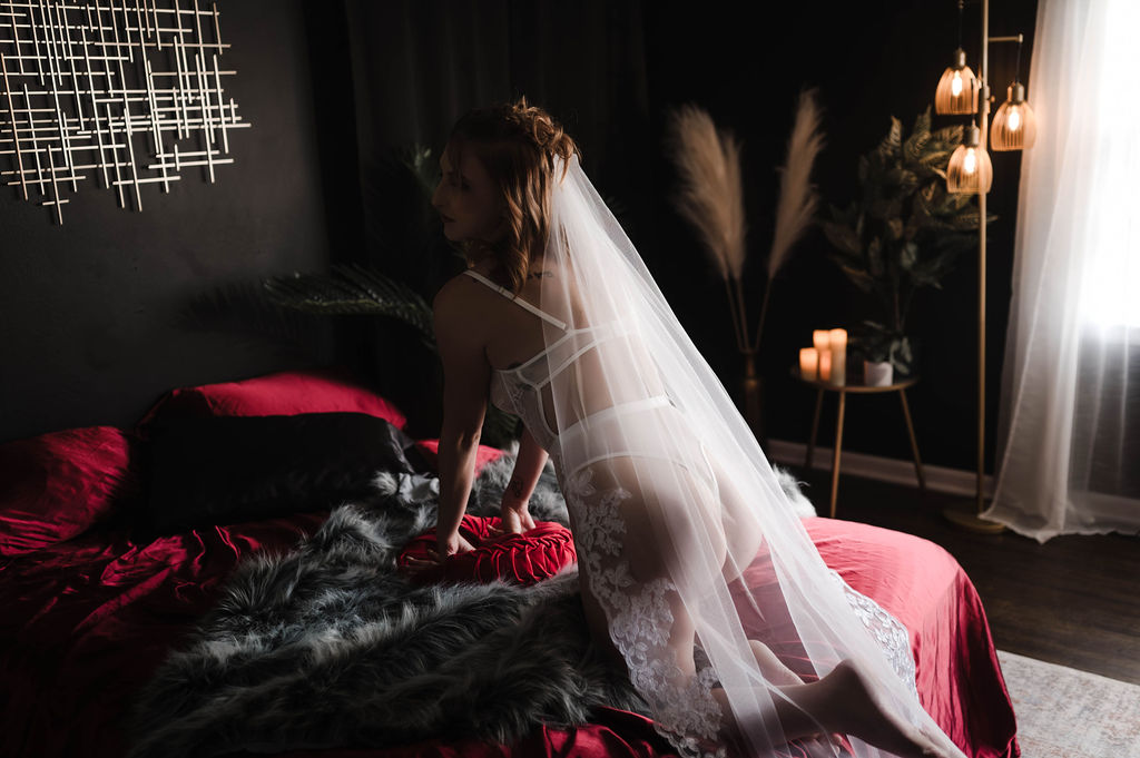 A woman in white lingerie crawls across a bed with red sheets in a studio