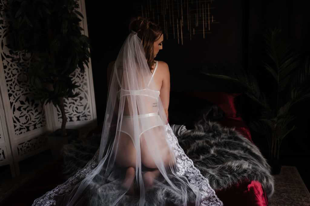 A woman in white lingerie and a long lace veil kneels on a bed in a studio after meeting marriage counselors memphis