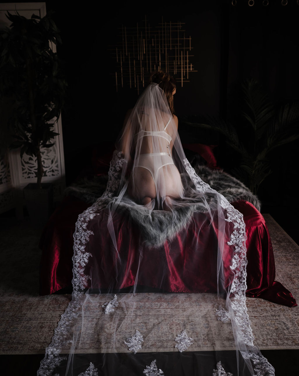 A bride in white lingerie and long veil kneels on a bed with red sheets after meeting with marriage counselors memphis