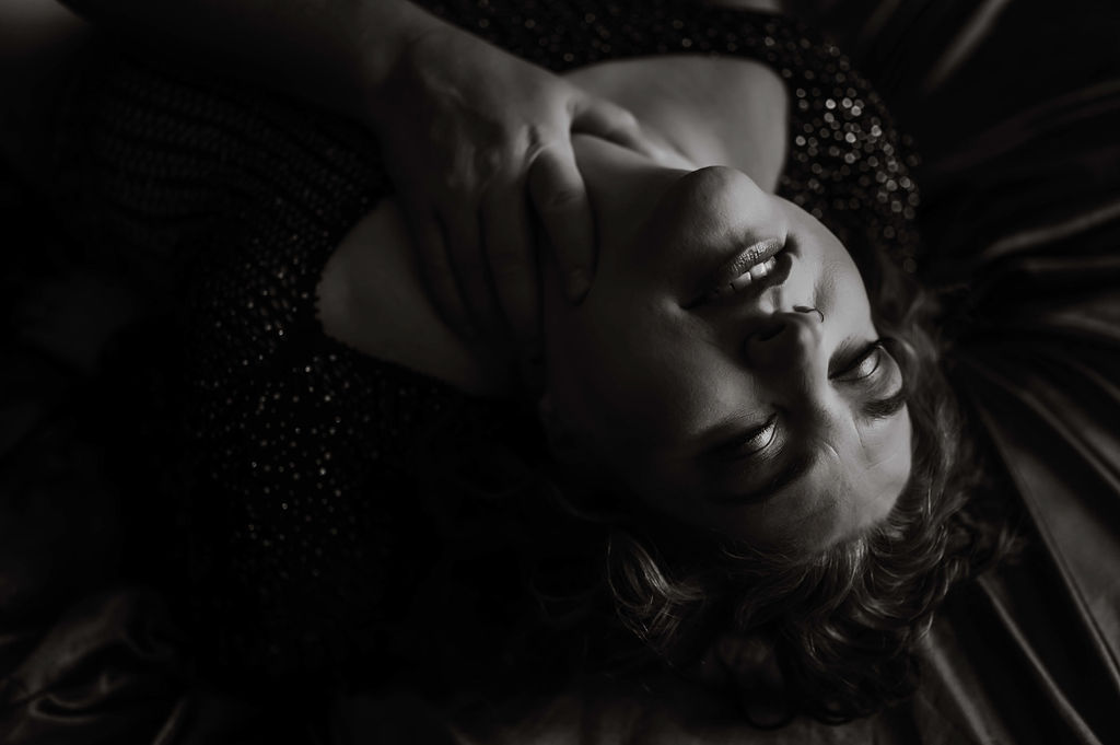 A woman leans back while laying on a bed with a hand on her neck