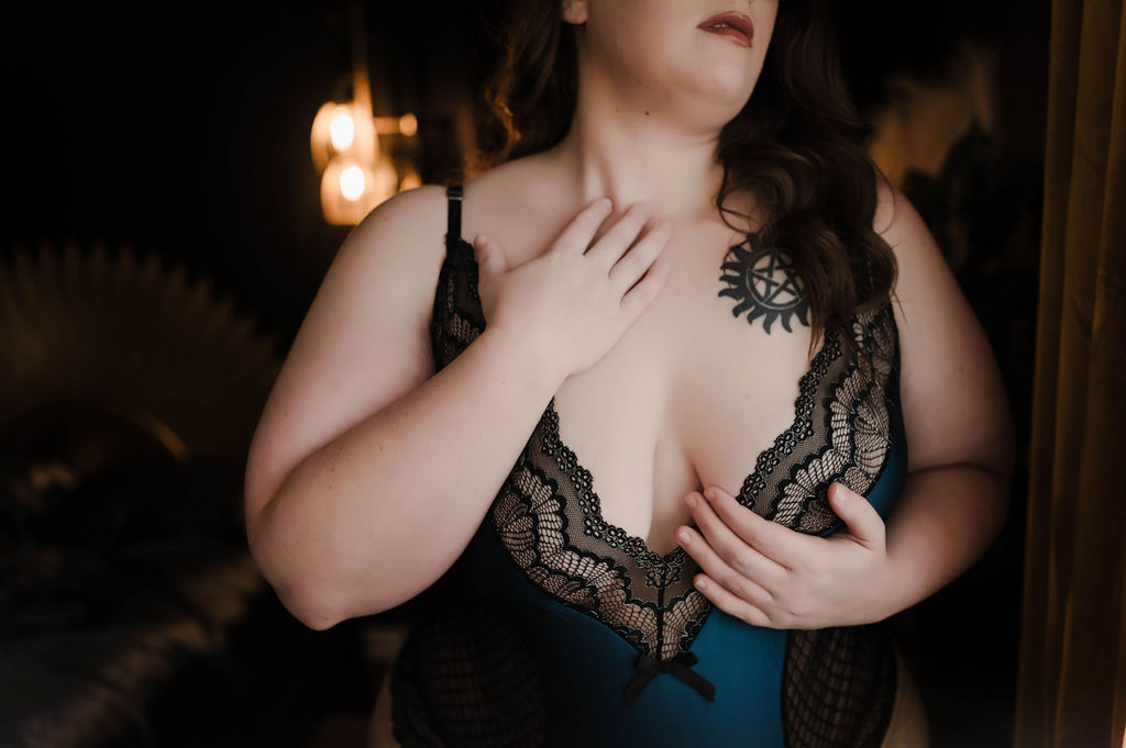 A woman caresses her neck and chest while standing in blue and black lingerie in a window after visiting spa collierville